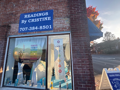 Readings By Cristine brick storefront on a Petaluma street with a blue sign and sidewalk board